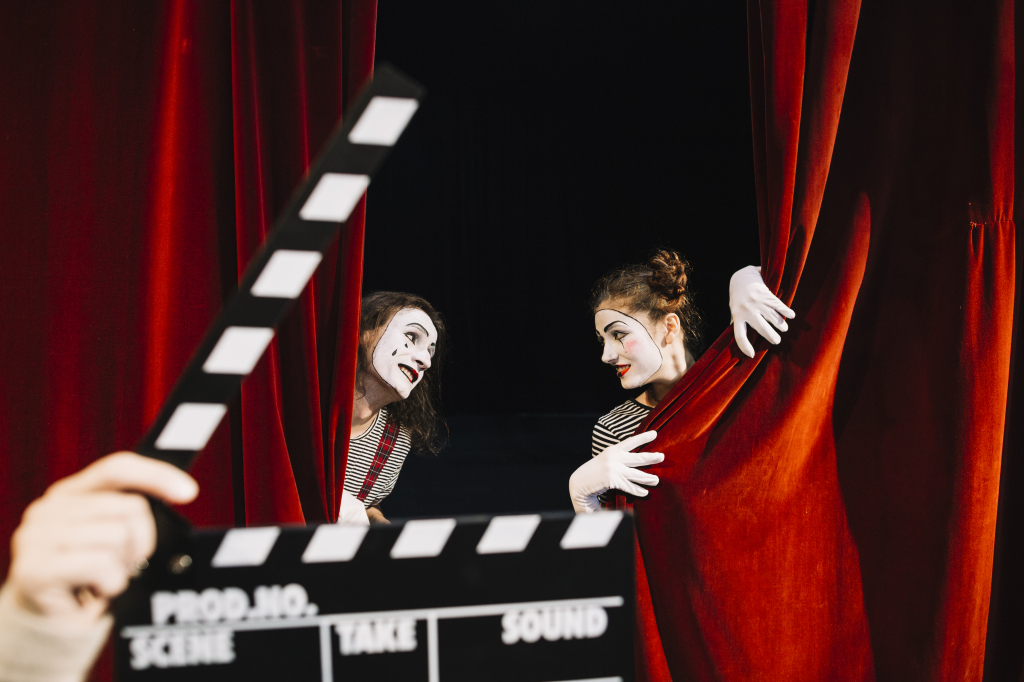 person-s-hand-holding-clapperboard-front-two-mime-artist-performing-red-curtain.jpg
