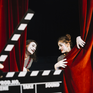 person-s-hand-holding-clapperboard-front-two-mime-artist-performing-red-curtain.jpg